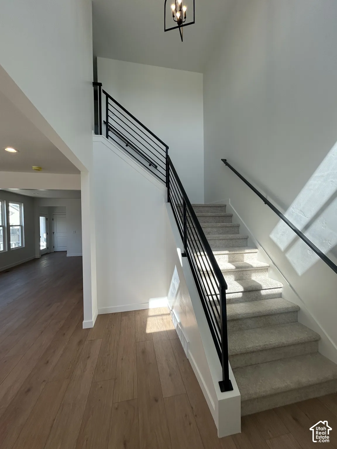 Two-story entryway featuring wood-finish flooring, a carpeted staircase with modern black metal balusters, a black metal handrail, and a contemporary ceiling light fixture
