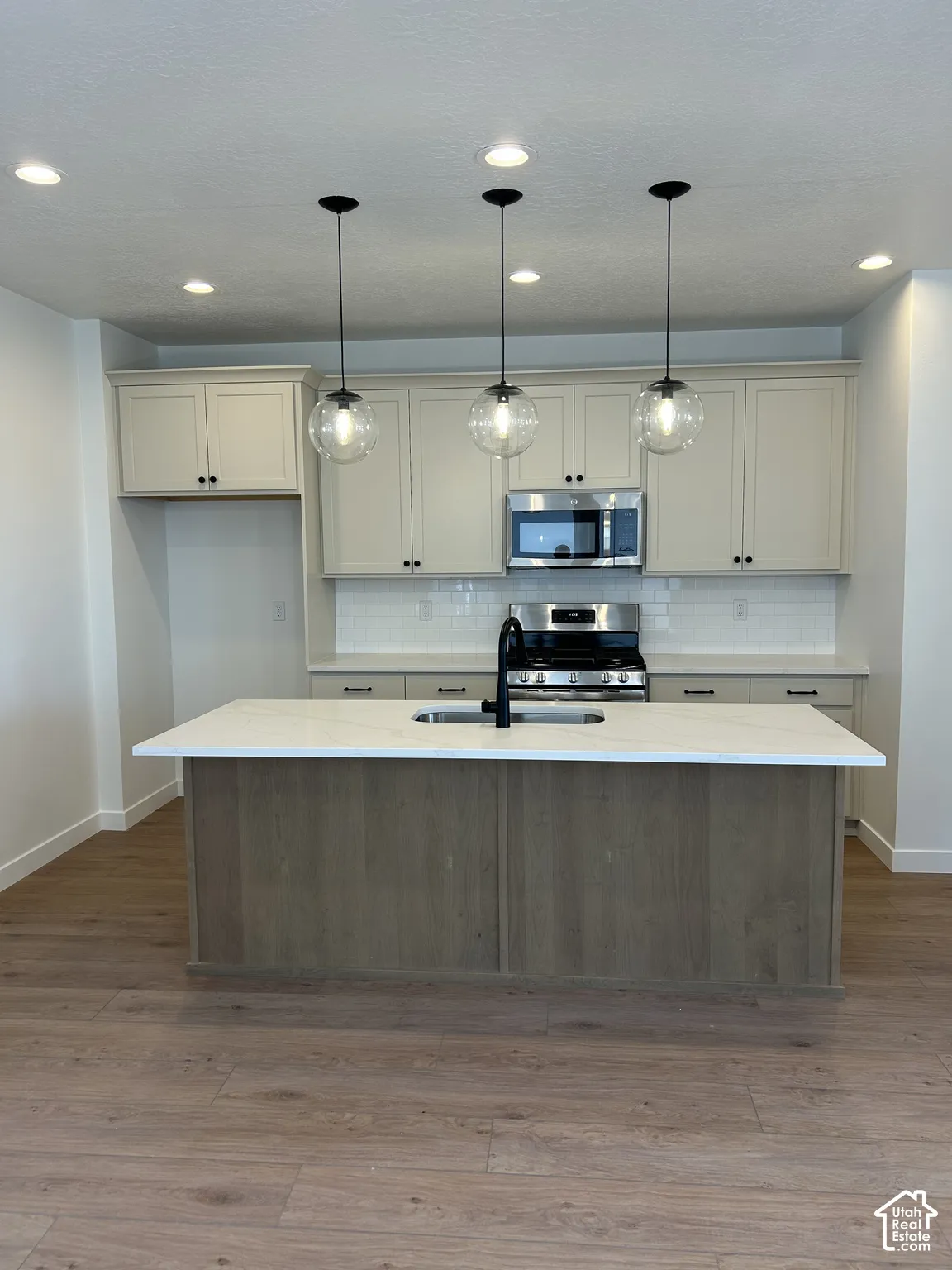 Kitchen featuring an island with a built-in sink, stainless steel appliances, wood-finish flooring, and recessed lighting