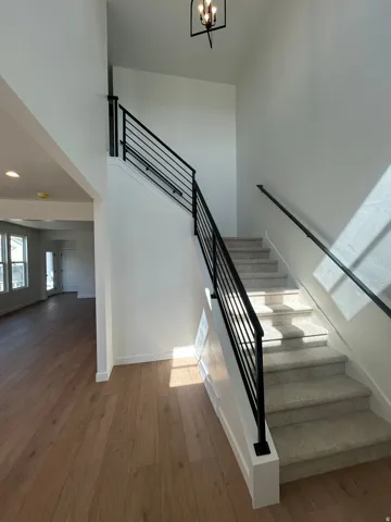 Two-story entryway featuring wood-finish flooring, a carpeted staircase with modern black metal balusters, a black metal handrail, and a contemporary ceiling light fixture
