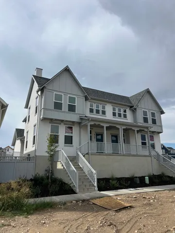 Multi-level exterior with light-toned stucco and vertical siding accents, featuring a covered porch with white railings, multiple windows, and a shingled roof