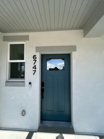 Contemporary entry door with transom window, stucco exterior, and horizontal paneling on the porch ceiling