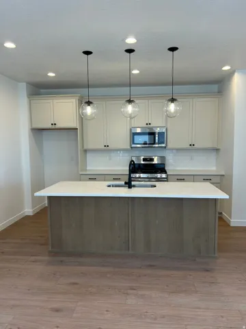 Kitchen featuring an island with a built-in sink, stainless steel appliances, wood-finish flooring, and recessed lighting