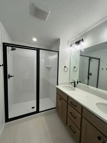 Walk-in shower with black-framed glass enclosure, double vanity with integrated sinks, wood-finish cabinetry, and contemporary black fixtures