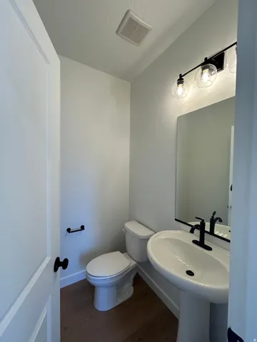 White pedestal sink with matte black faucet and coordinating wall-mounted light fixture