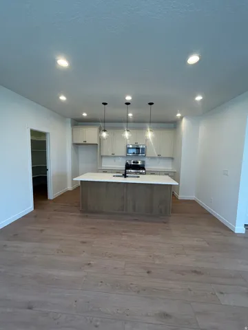 Open-concept kitchen featuring an island with built-in sink, pendant lighting, recessed lighting, white cabinetry, and wood-finish flooring