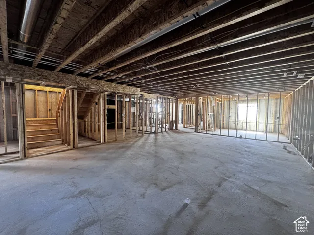 Unfinished basement featuring exposed wood joists, structural framing, concrete flooring, and a visible stairwell
