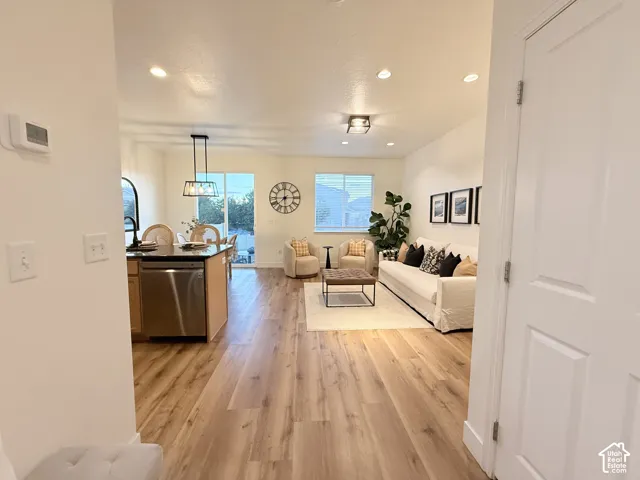 Open-concept living space with wood-finish flooring, recessed lighting, and a kitchen island featuring a stainless steel dishwasher