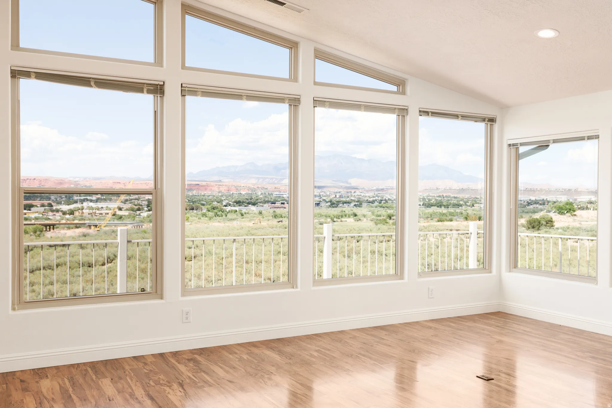 Expansive windows with mountain scenery, vaulted ceiling, recessed lighting, and wood-finish flooring