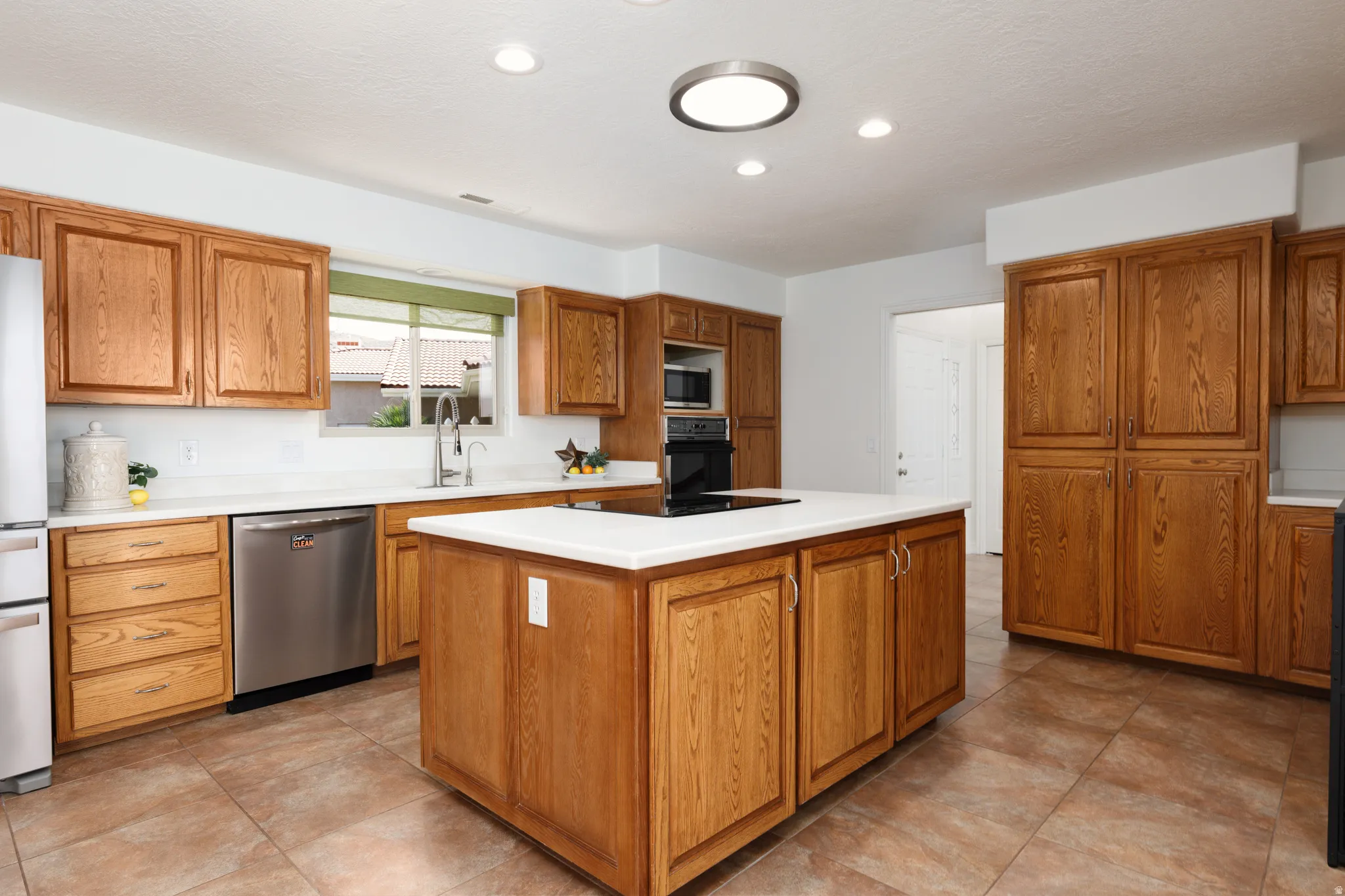 Kitchen featuring wood-finish cabinetry, stainless steel appliances, a center island with a cooktop, white countertops, and tile flooring