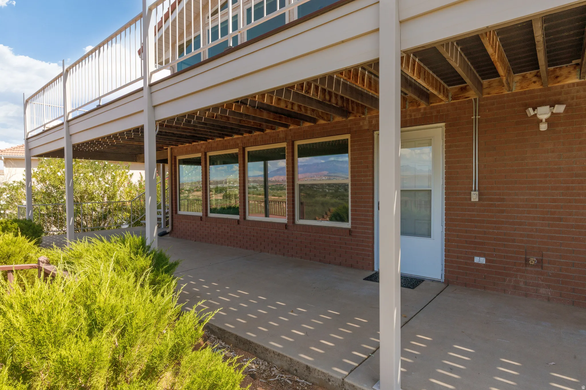 Covered patio with a brick exterior, multiple windows, and a glass-paneled door