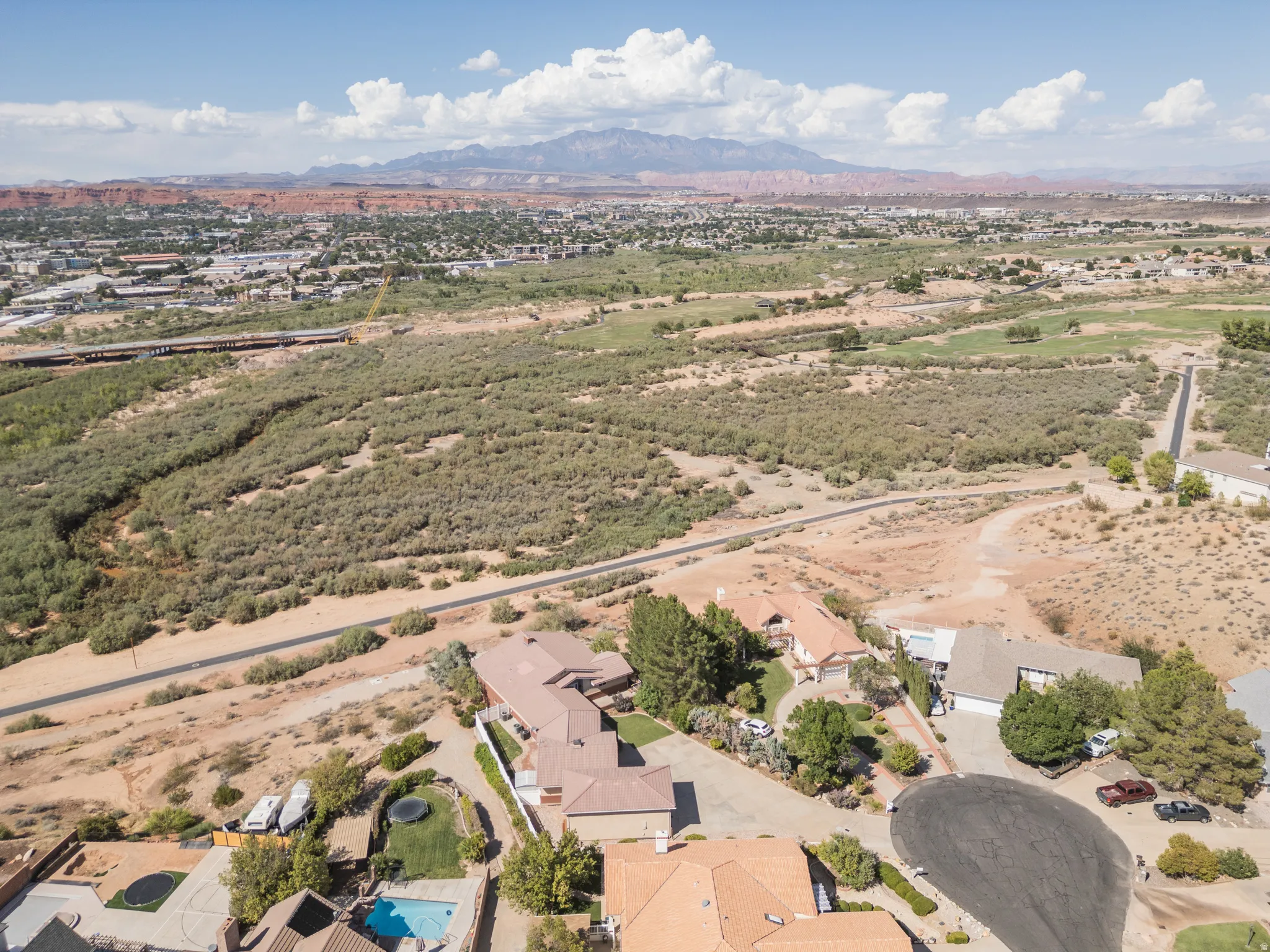Aerial perspective showcasing a residential neighborhood, expansive arid landscape, distant mountains, and a clear sky with scattered clouds
