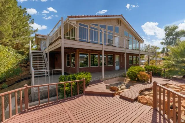 Multi-level dwelling with a large upper-level balcony featuring glass railings, a lower-level patio, and a deck with wooden pathways