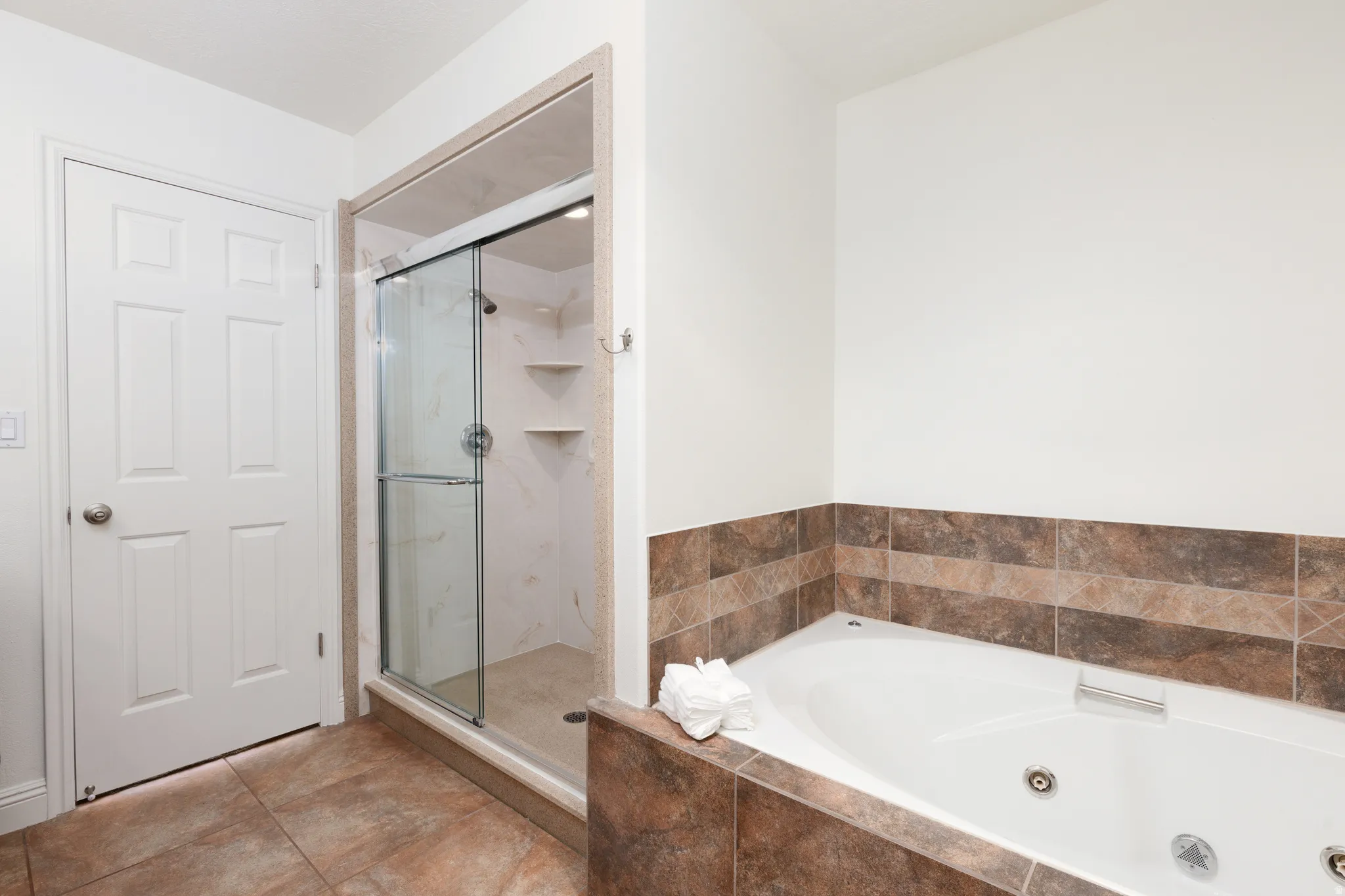 Tiled flooring, glass-enclosed shower with tiled walls and built-in shelving, white paneled door, and a built-in tub with tiled surround