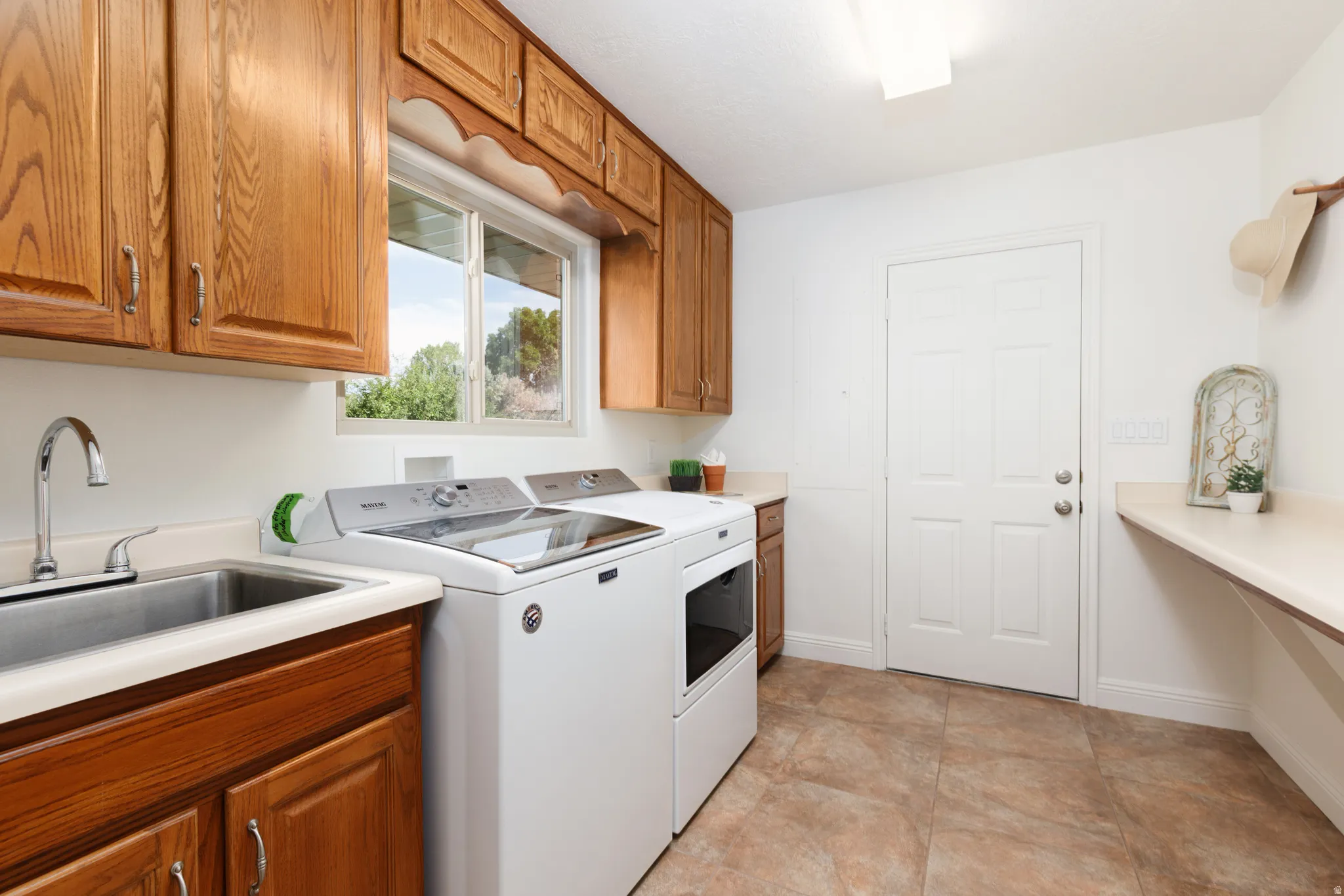 Laundry room featuring wood-finish cabinetry, a utility sink with a chrome faucet, a functional window, and a built-in wall shelf