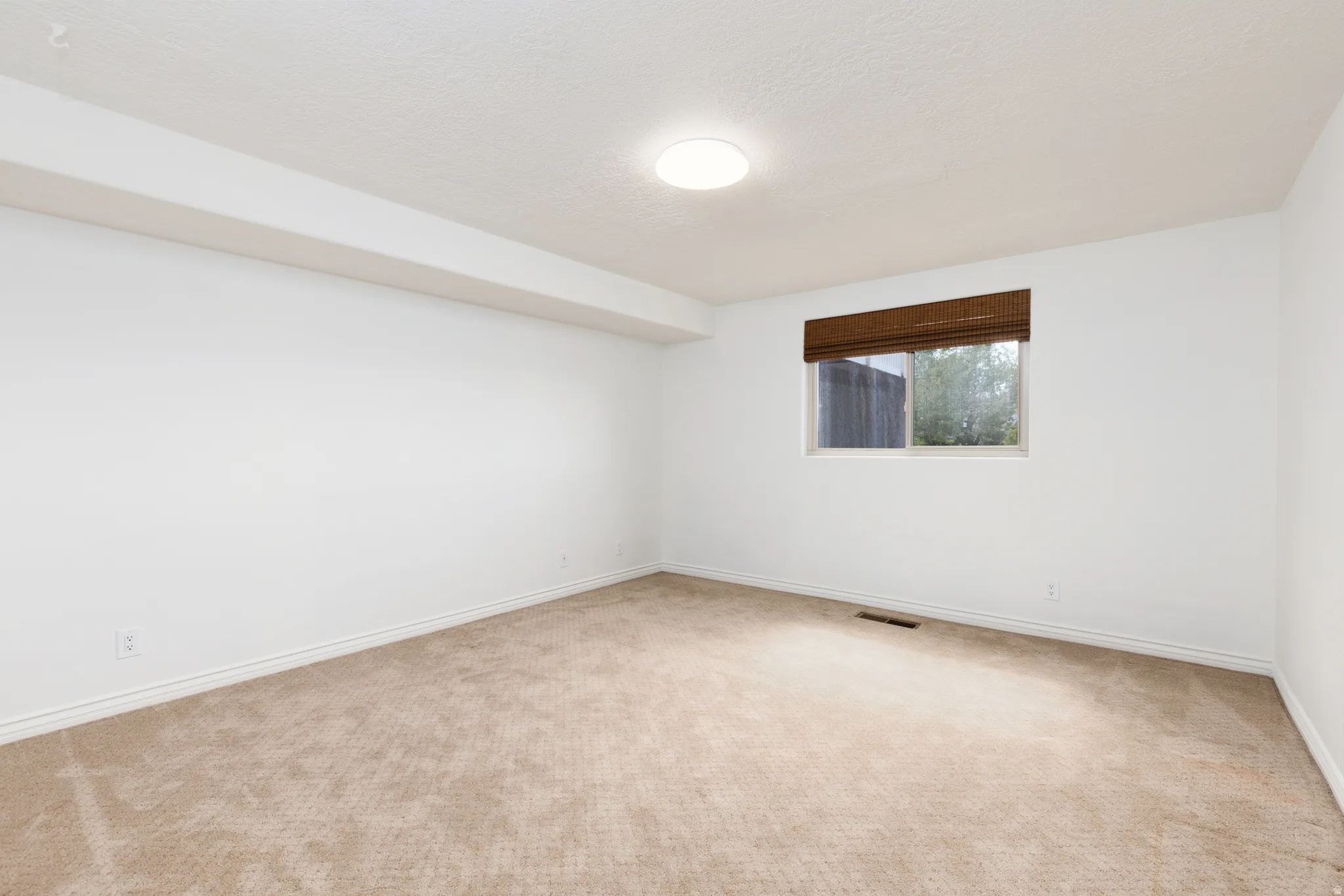 Bedroom 5 Neutral tone wall finish, plush carpeting, recessed lighting, and a single window with a woven shade