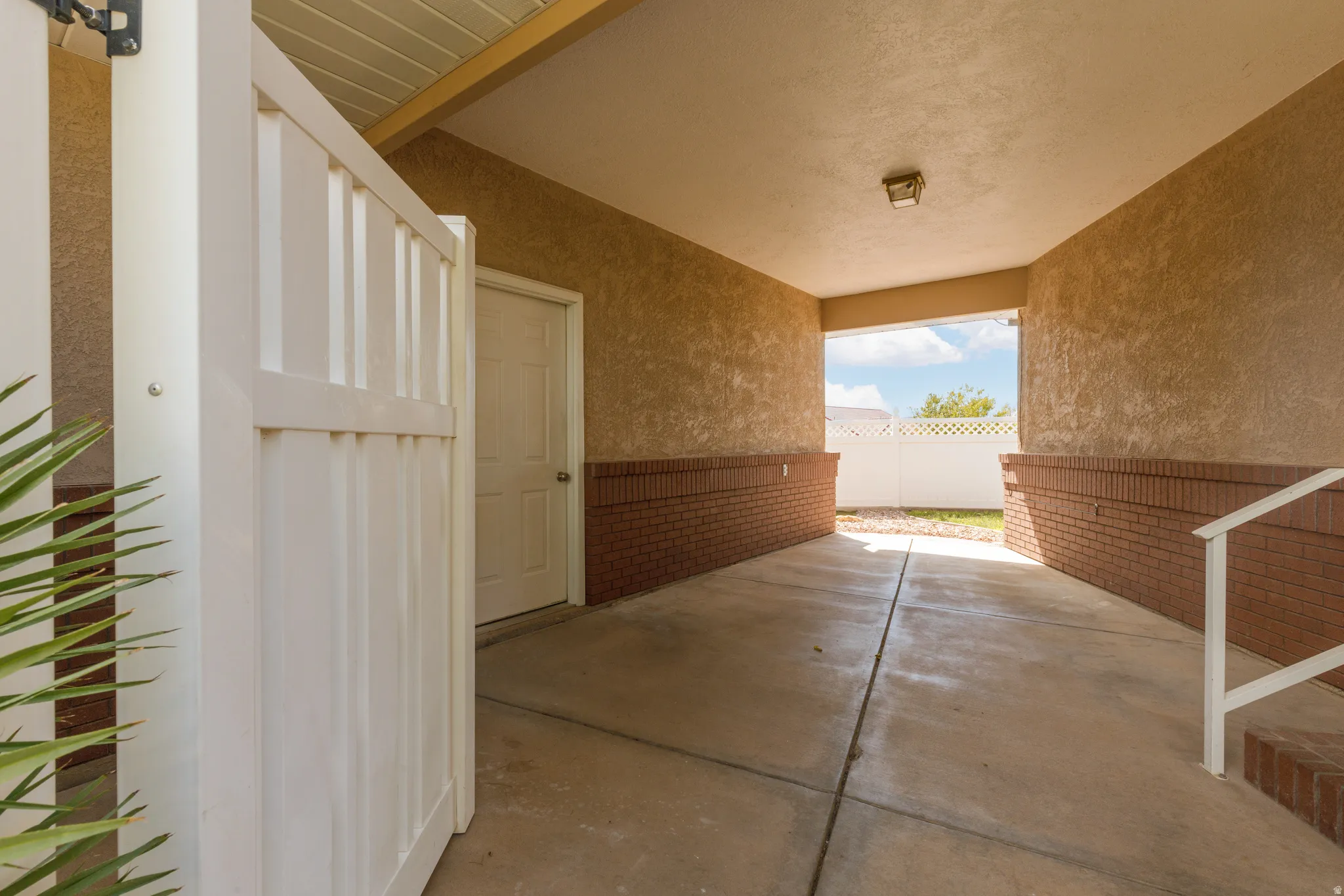 Covered breezeway between house and garage with stucco walls, brick wainscoting, and a white privacy gate