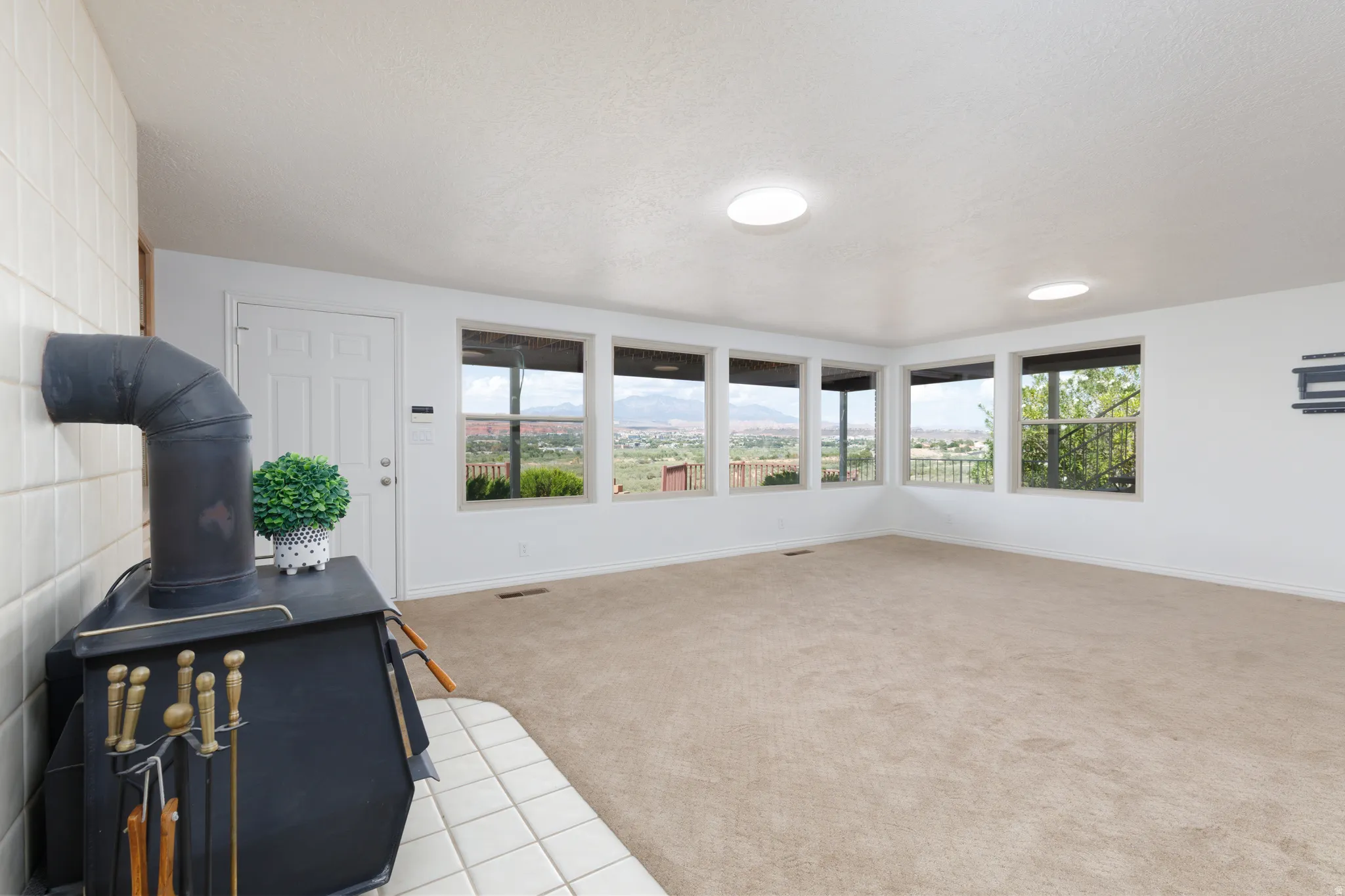 Wood-burning stove with a tiled hearth and wall, recessed lighting, and expansive windows