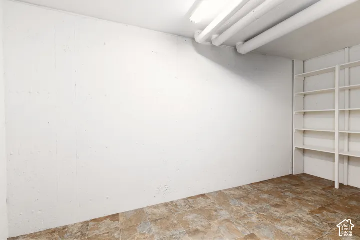 Second storage are with wall-mounted built-in shelving, tiled flooring, exposed ceiling pipes, and fluorescent lighting