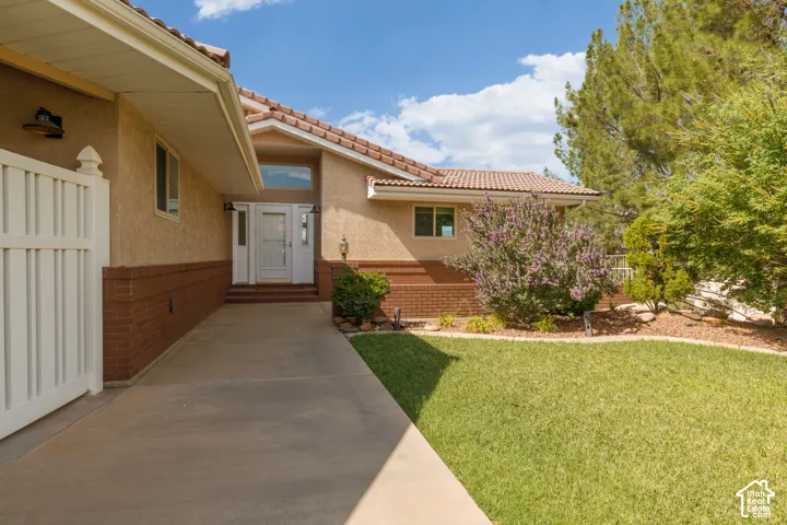 Stucco exterior with brick detailing, tile roofing, concrete walkway, white entry door with side lights, and mature landscaping