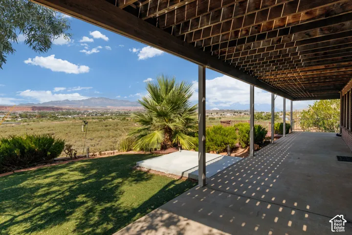 Expansive covered patio with concrete flooring, supported by multiple columns, overlooking turf lawn and distant mountain range