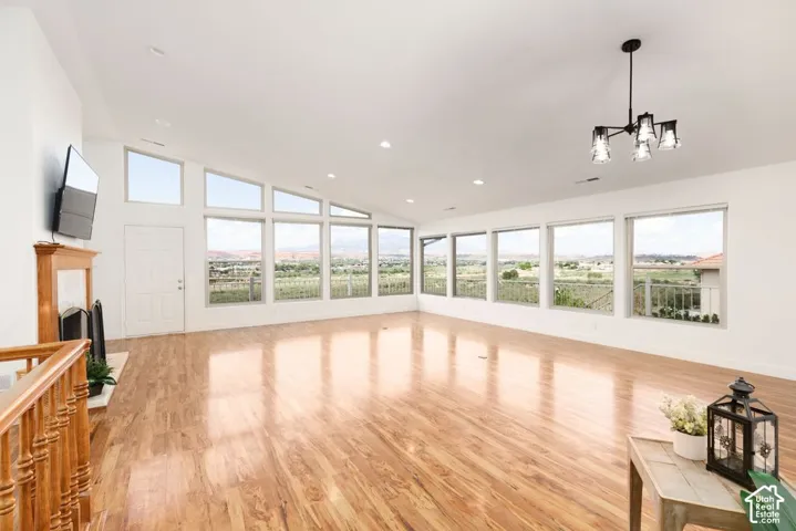 Vaulted ceiling, wood-finish flooring, multiple expansive windows, fireplace with wood mantel, and a black-finish chandelier