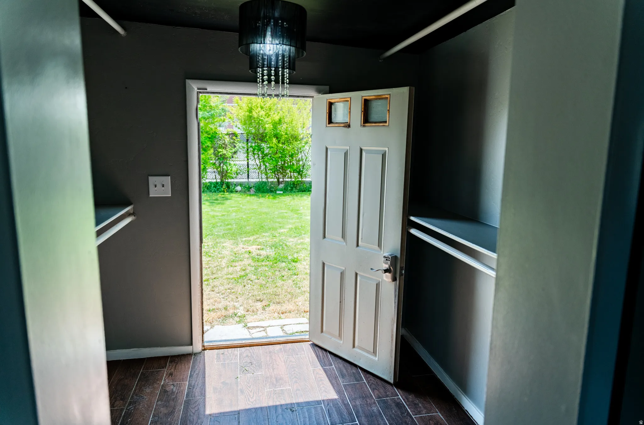 Wood-finish flooring, built-in shelving, chandelier lighting, paneled door with window accents, and a manicured lawn