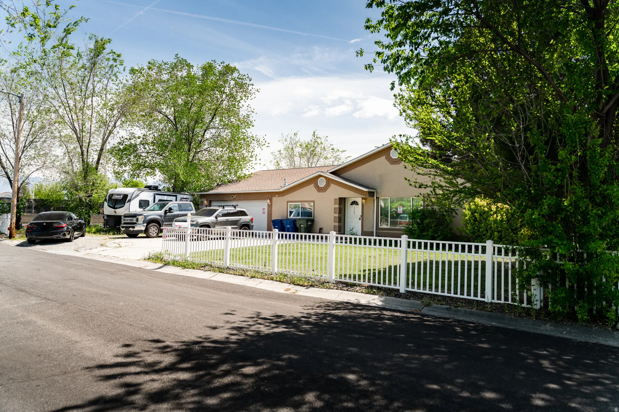 Single-story residence featuring a tan stucco exterior, an attached garage, and a white picket fence enclosing a front lawn