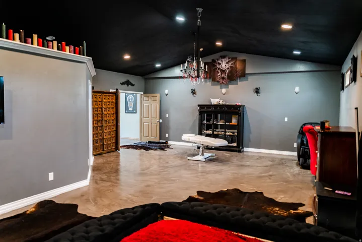 Vaulted ceiling with recessed lighting, polished concrete flooring, double entry doors, wall-mounted sconces, and a decorative chandelier