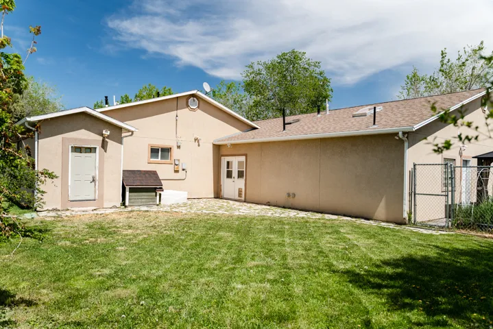 Expansive rear yard featuring a paved patio area, stucco exterior, and a chain-link fence