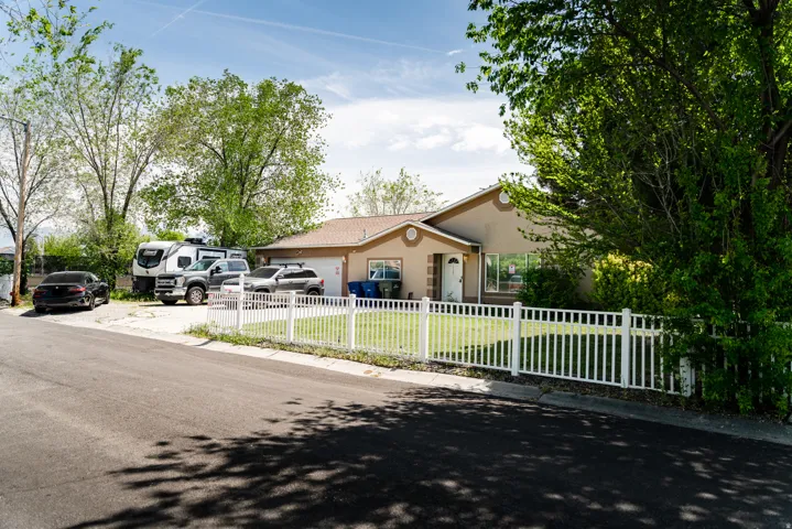 Single-story residence featuring a tan stucco exterior, an attached garage, and a white picket fence enclosing a front lawn