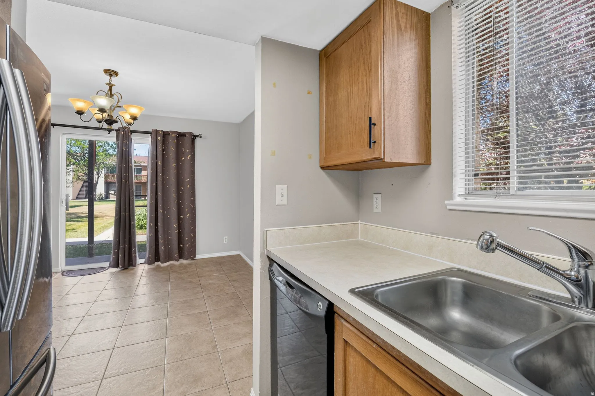 Kitchen featuring a double basin stainless steel sink, a kitchen window, wood-finish cabinetry, and a dishwasher