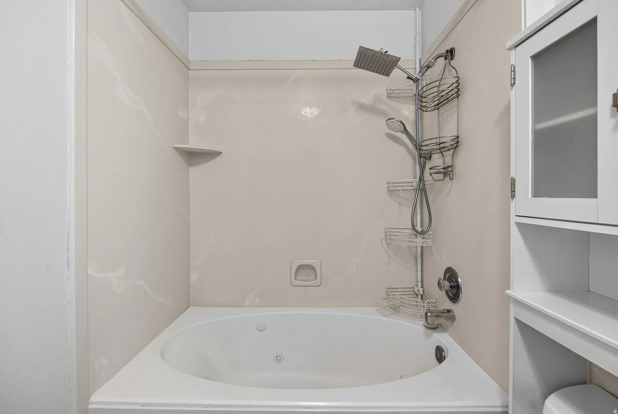 Alcove bathtub with integrated jets, corner shelf, and a white tile surround