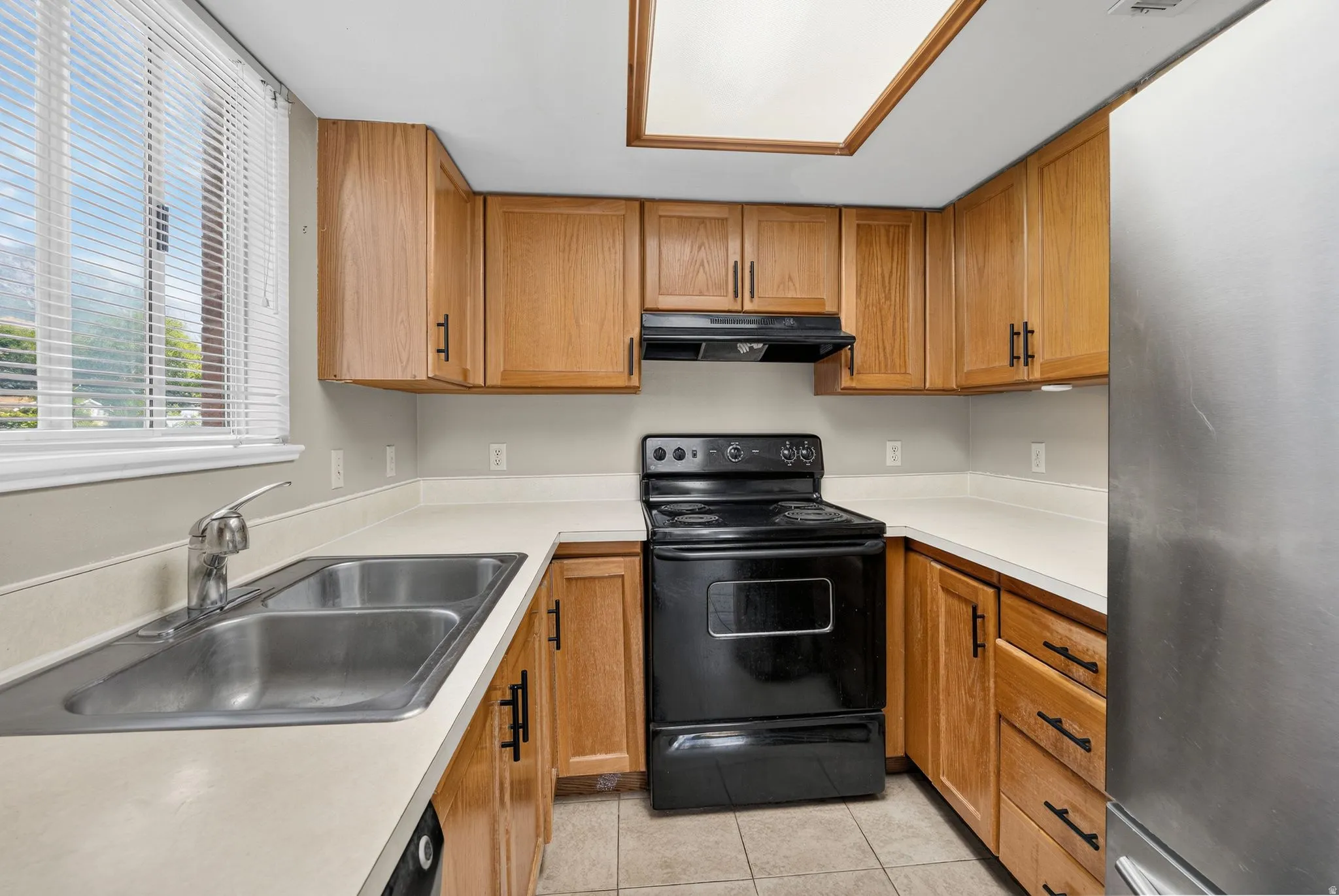 Kitchen featuring wood cabinetry, light-toned countertops, a stainless steel sink, and tile flooring