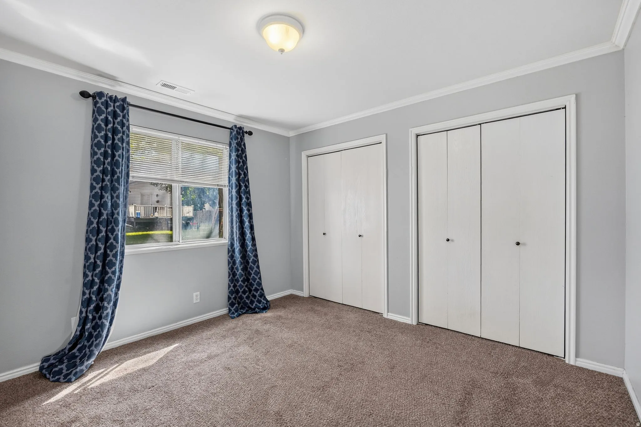 Recessed window with blinds, two bi-fold closet doors, wall-to-wall carpeting, and crown molding