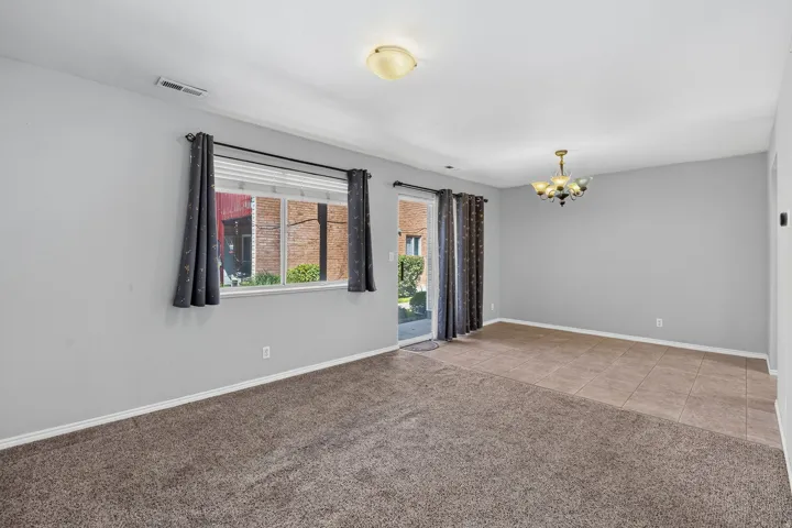 Carpeted flooring, tile flooring, glass sliding door, window with blinds, and a decorative ceiling light fixture