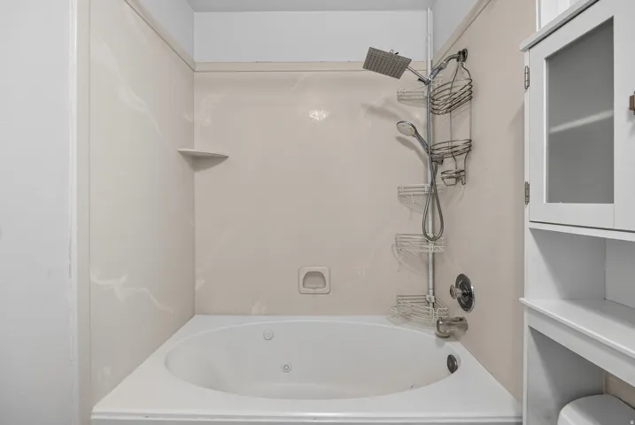 Alcove bathtub with integrated jets, corner shelf, and a white tile surround
