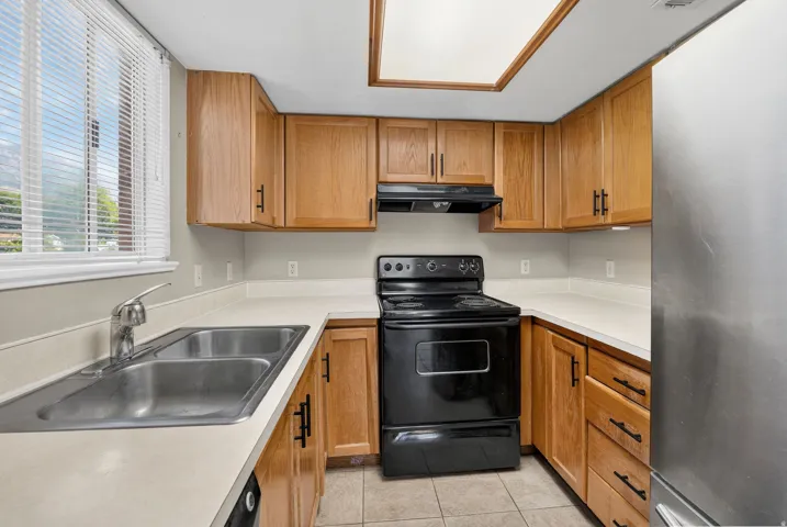 Kitchen featuring wood cabinetry, light-toned countertops, a stainless steel sink, and tile flooring