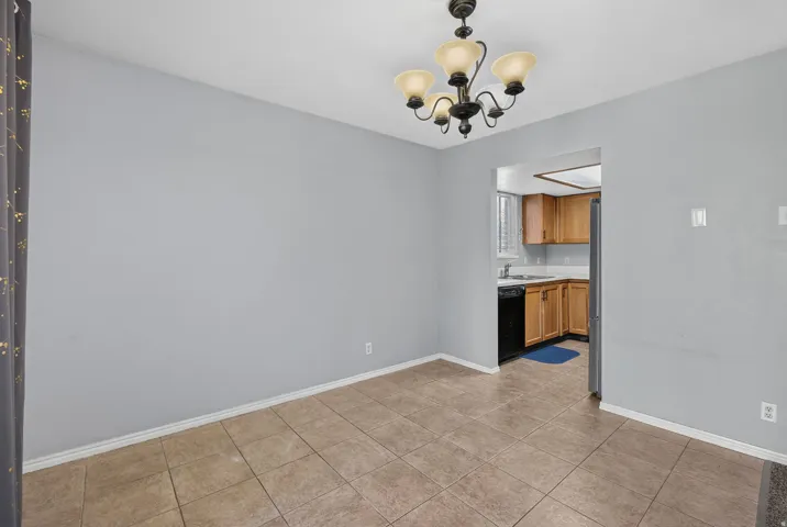 Tile flooring extending into the kitchen, kitchen with wood-finish cabinetry, black appliances, and white countertops