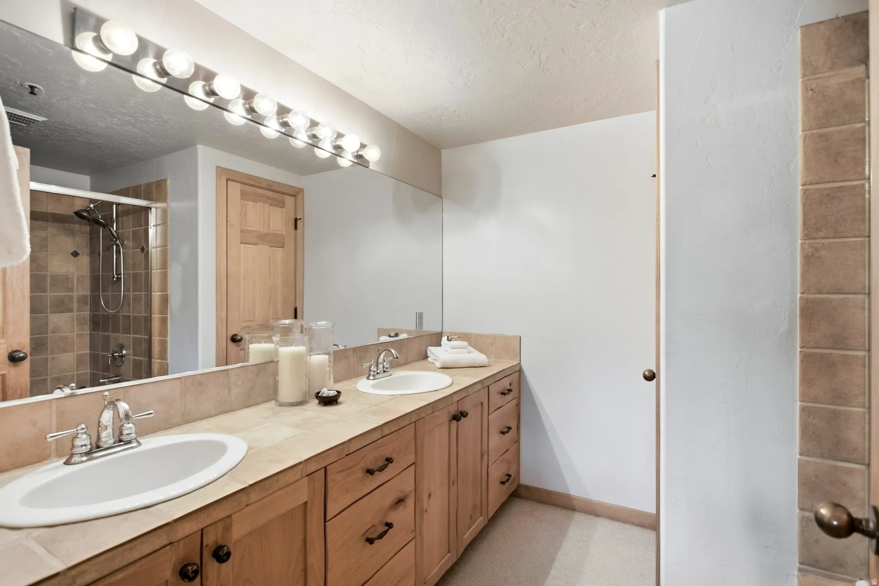 Double vanity with integrated sinks, wood cabinetry, tile countertop, and a tiled shower enclosure