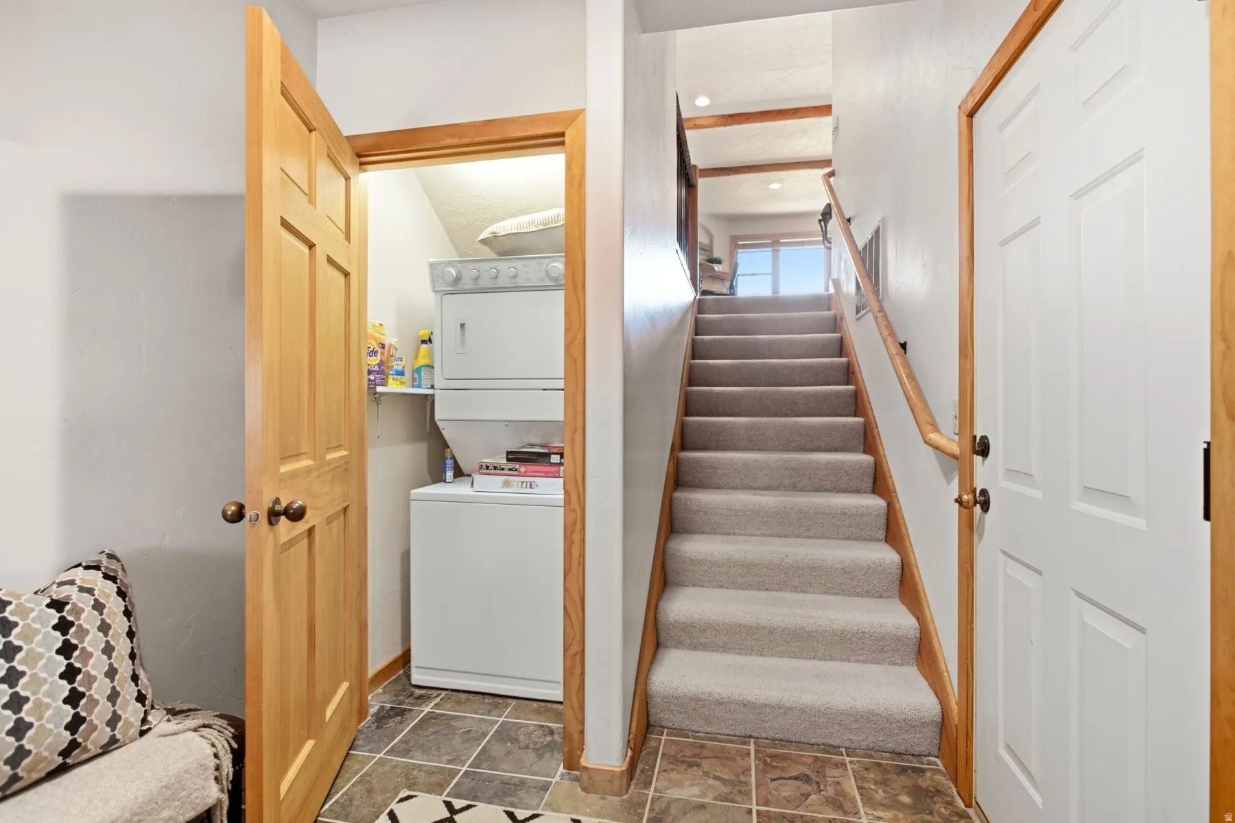 Dedicated laundry area with stacked white appliances, wood-finish trim, and tile flooring