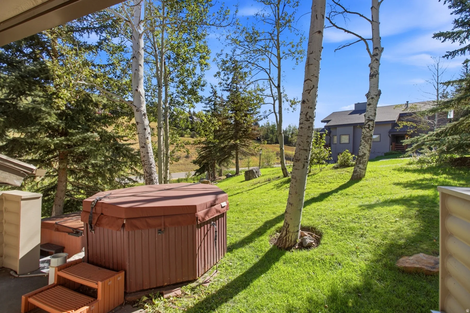 Outdoor patio featuring two spa tubs, slatted wood steps, and a grassy area with mature trees