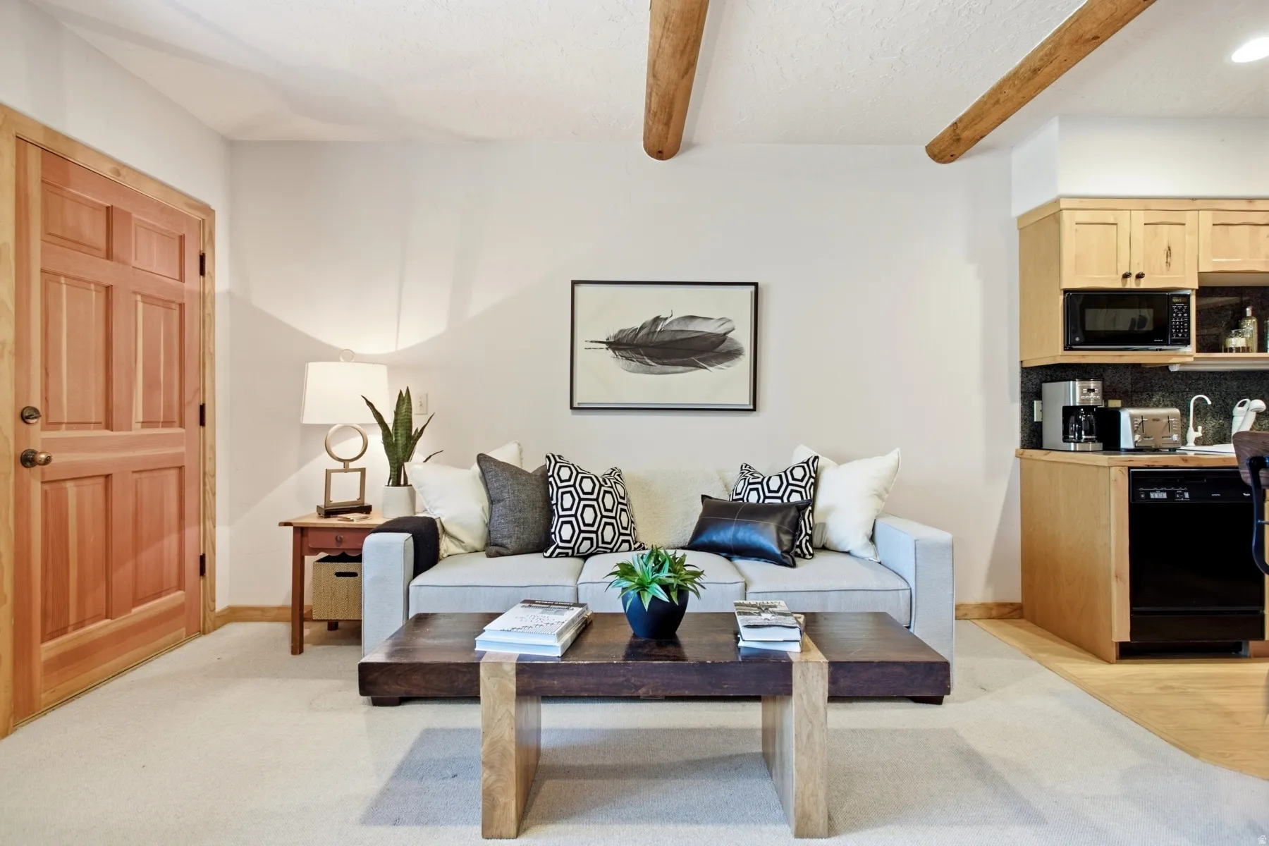 Exposed ceiling beams, natural wood door, integrated kitchenette, light-toned wall finishes, and carpeted flooring