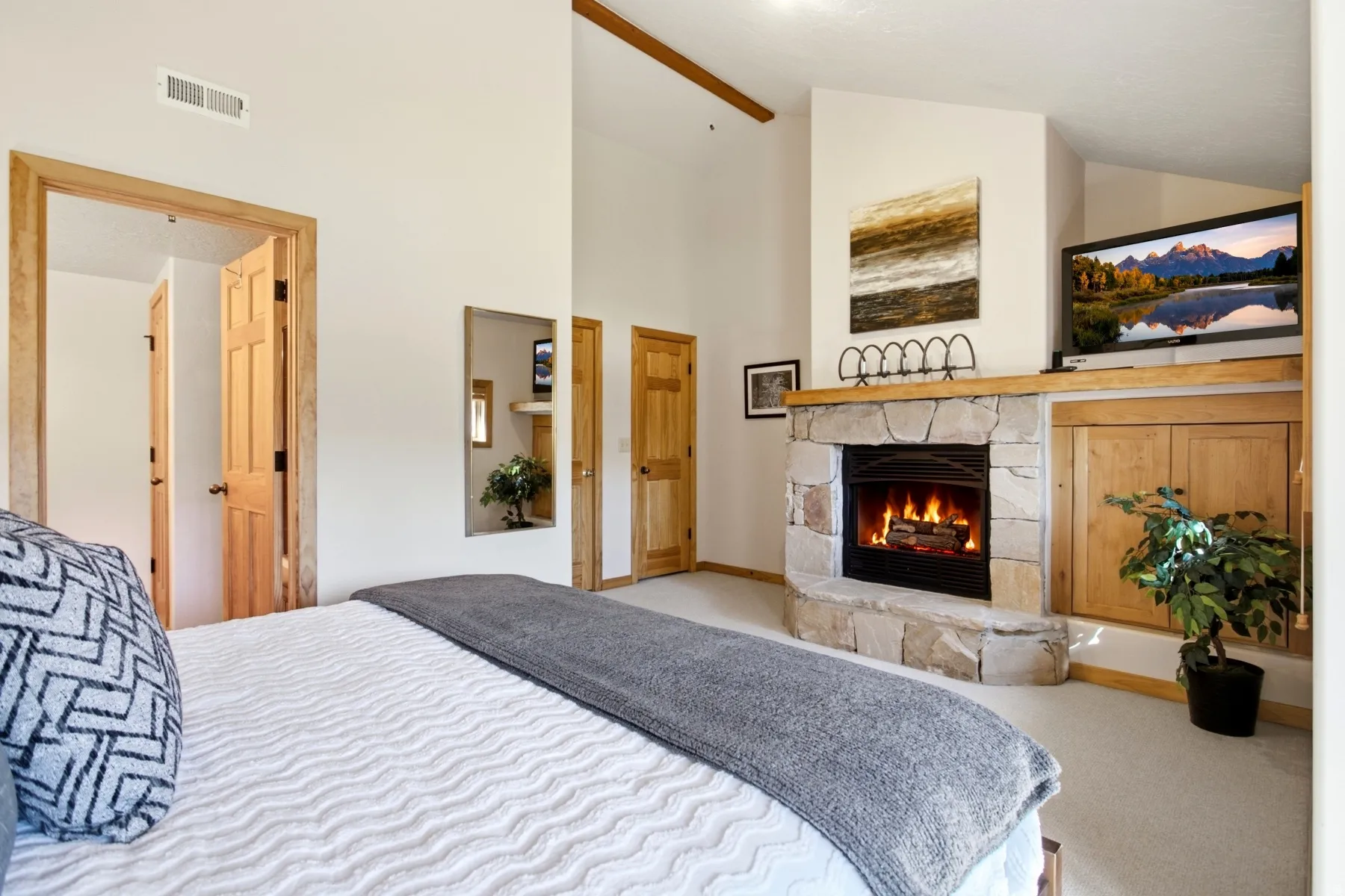 Corner stone fireplace with wood mantel, vaulted ceiling with exposed wood beam, natural wood doors, and built-in wood cabinetry
