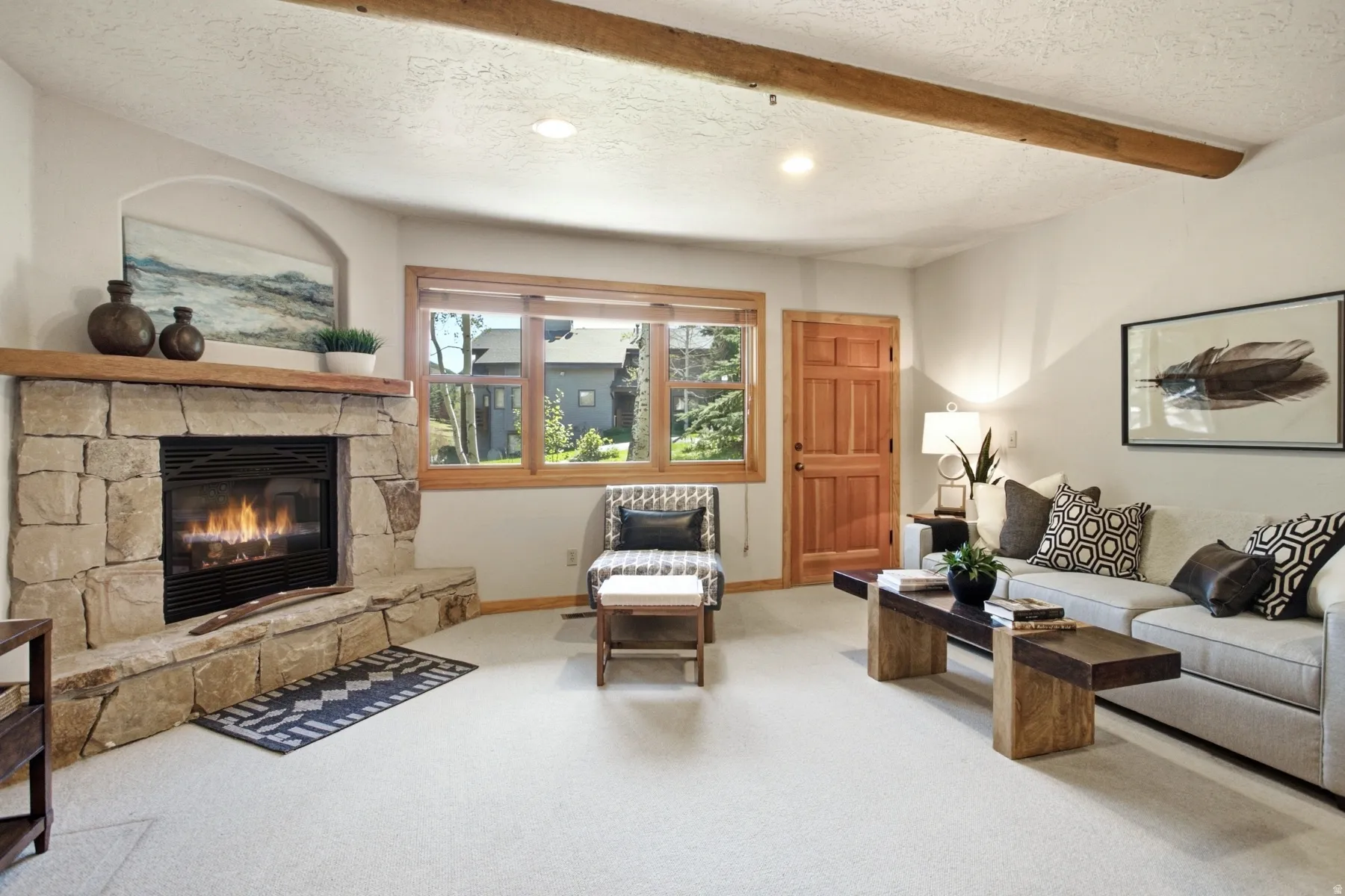 Stone-faced fireplace with a wood mantel, wood-framed window, wood door, exposed ceiling beam, and recessed lighting