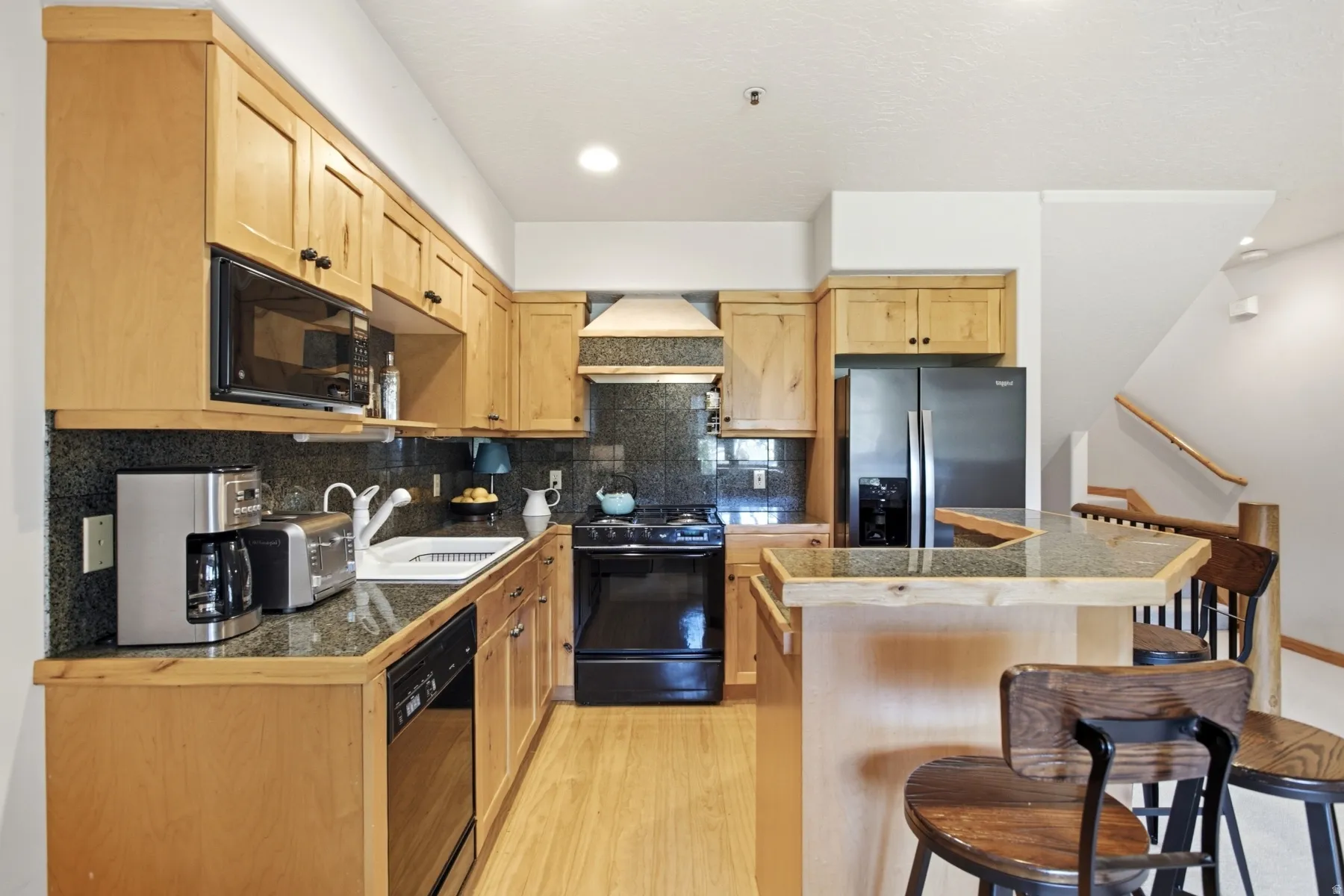 Kitchen featuring wood-finish cabinetry, dark countertops, built-in microwave, integrated dishwasher, and a breakfast bar with a stone-finish surface
