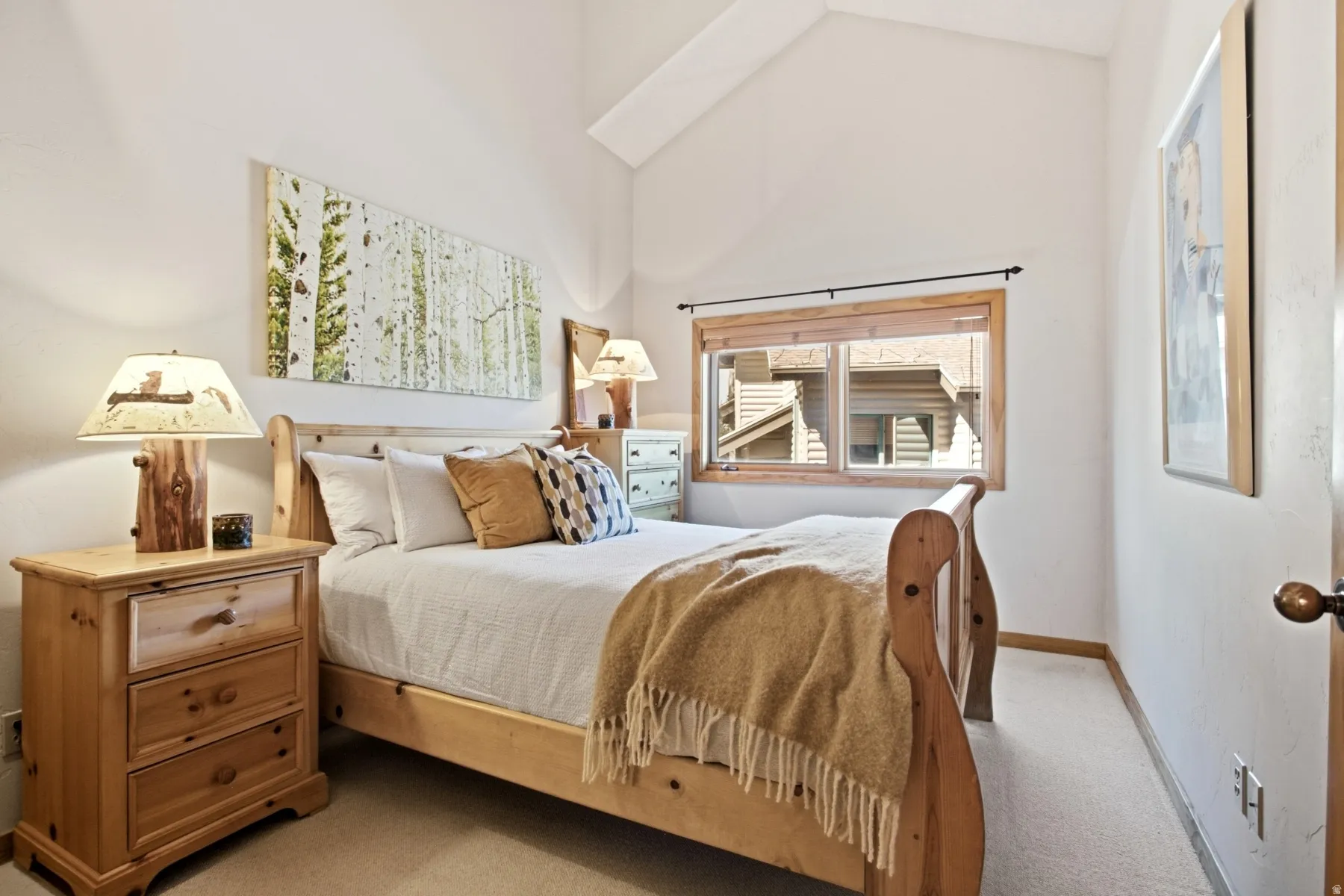 Vaulted ceiling, wood-frame window, light-toned walls, and neutral carpeting