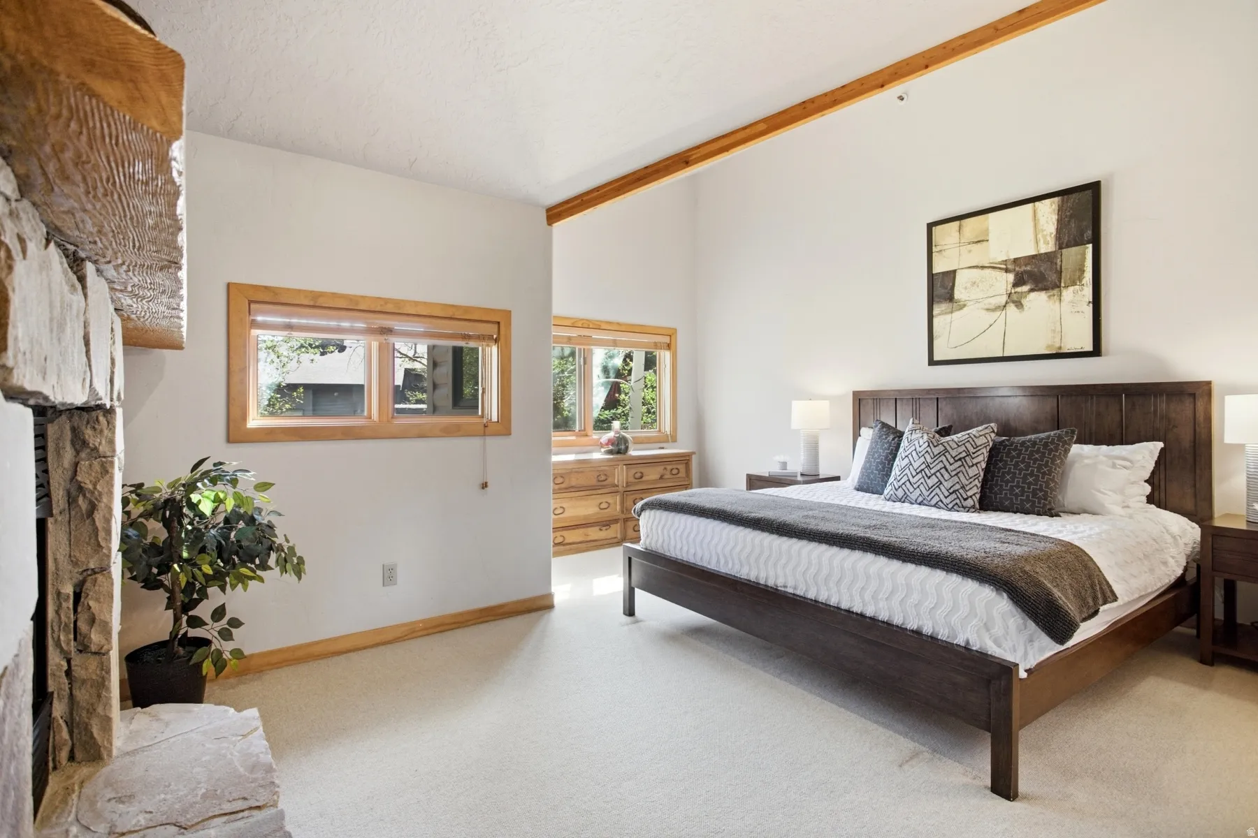 Vaulted ceiling with exposed wood beams, light wood-trimmed windows, and a stone-clad fireplace