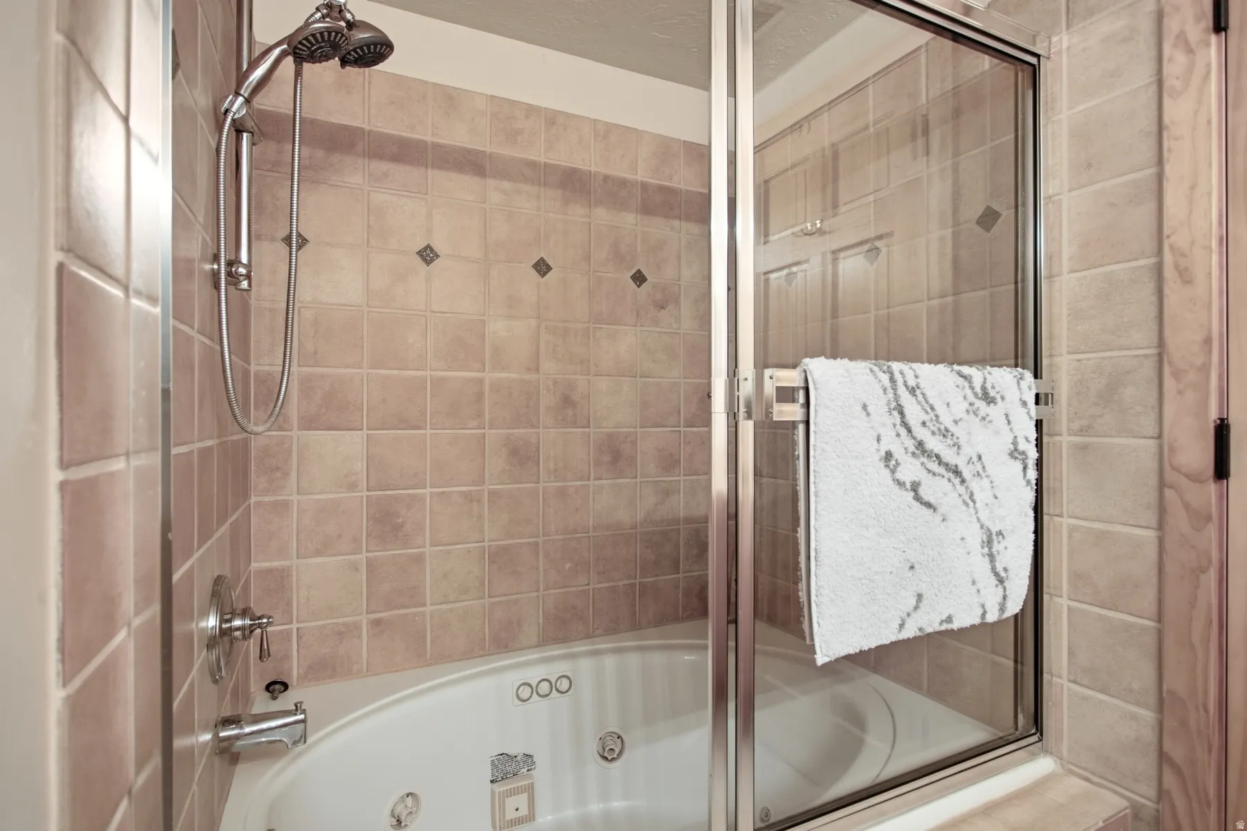 Tile-surround corner bathtub with integrated jets, featuring a handheld shower fixture