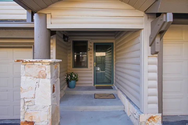 Entryway featuring stone column, covered porch, horizontal siding, and a paneled garage door