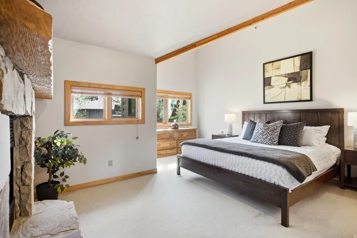 Vaulted ceiling with exposed wood beams, light wood-trimmed windows, and a stone-clad fireplace